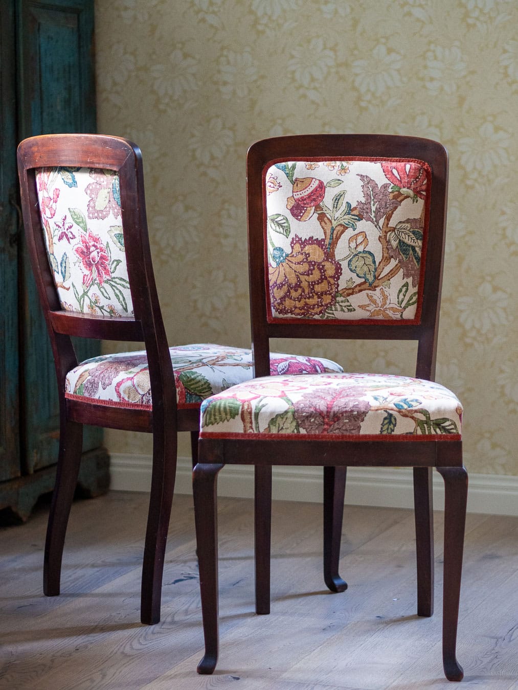 Kaksi vanhaa pikkutuolia verhoiltuna kukkakankaalla.
